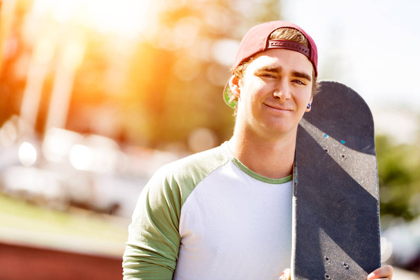 Teenage boy with skateboard standing outdoors - Fotó, kép