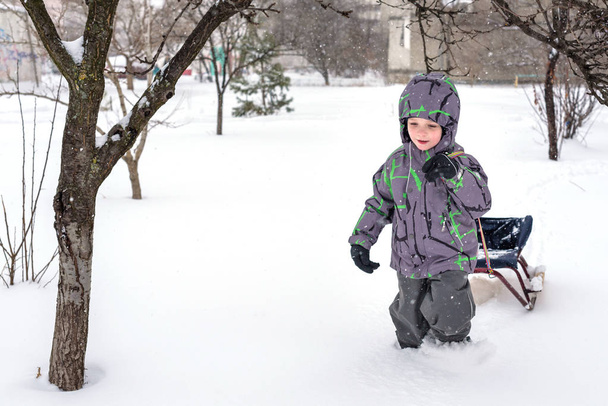 Happy kid walking outdoors in winter city drags his sled. child  - Photo, Image