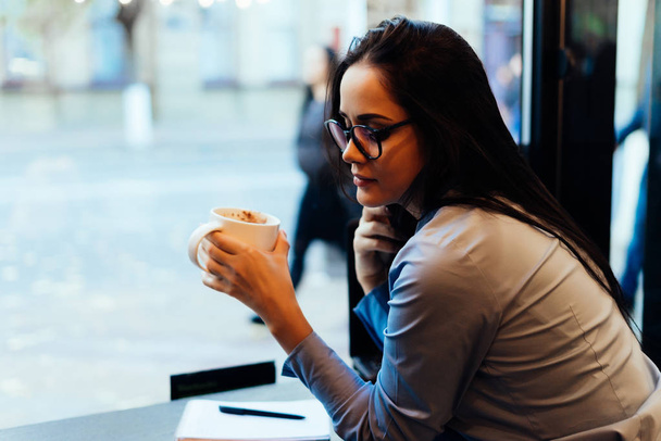 pensive young girl student sitting in cafe after class and drinking coffee - Фото, изображение
