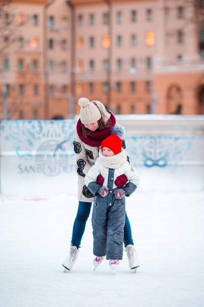 Schattig meisje met haar moeder schaatsen op de ijsbaan - Foto, afbeelding