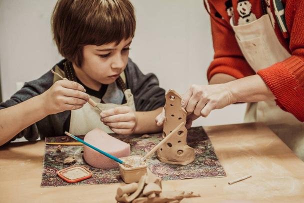 El niño se dedica a una escuela de cerámica, esculpe un producto de arcilla
 - Foto, Imagen