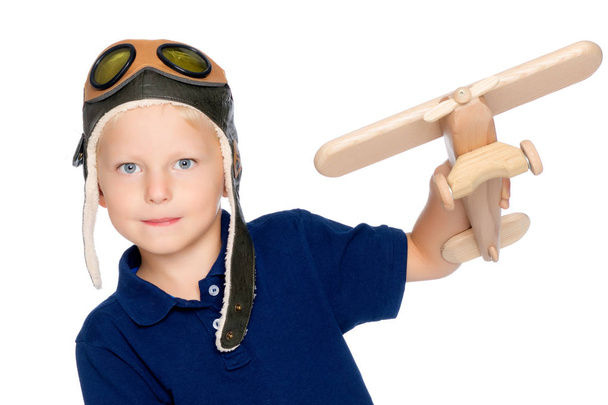 Um menino em um boné de pilotos e um avião de madeira em sua mão
 - Foto, Imagem