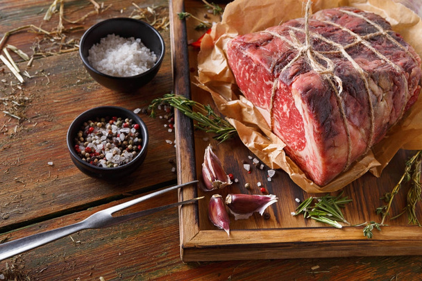 Raw aged prime black angus beef in craft papper on rustic wood - Foto, Imagen