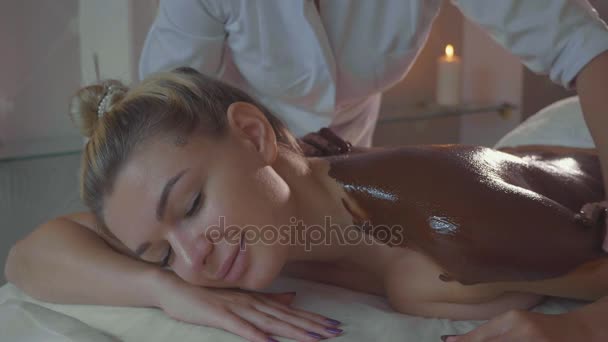 Beautician doing massage with chocolate to young beautiful woman at spa salon - Footage, Video