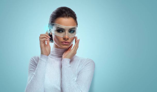An attractive brunette model in futuristic office with virtual holographic glasses, smooth background with copyspac - Fotoğraf, Görsel