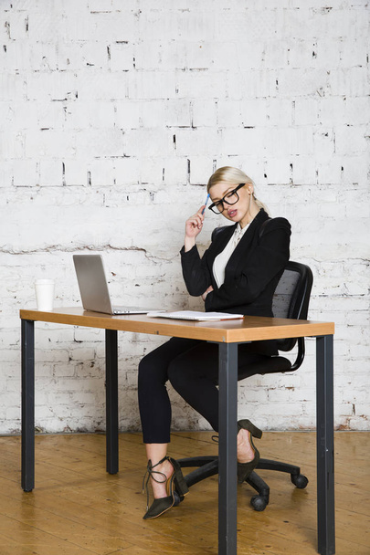 Young blond beauty businesswoman sitting at a office table with laptop, notebook and glasses in suit. Business concept. - Foto, Imagen