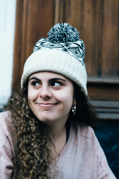 Улыбающаяся девочка-подросток с длинными и вьющимися волосами в вязаной шляпе
 - Фото, изображение