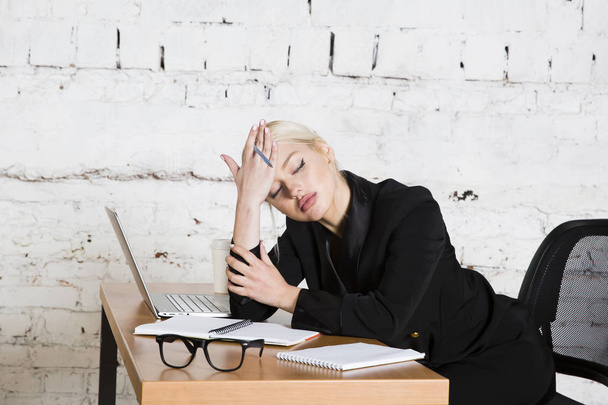 Jovem mulher de negócios de beleza loira sentada em uma mesa de escritório com laptop, notebook e óculos de terno. Conceito de negócio
. - Foto, Imagem