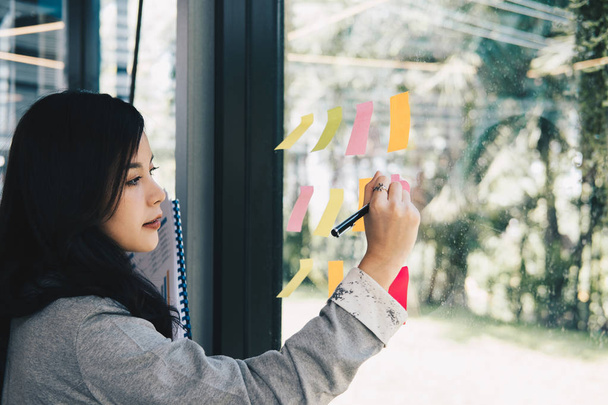 Geschäftsfrau schreibt in Besprechung auf Klebezettel an Glaswand - Foto, Bild