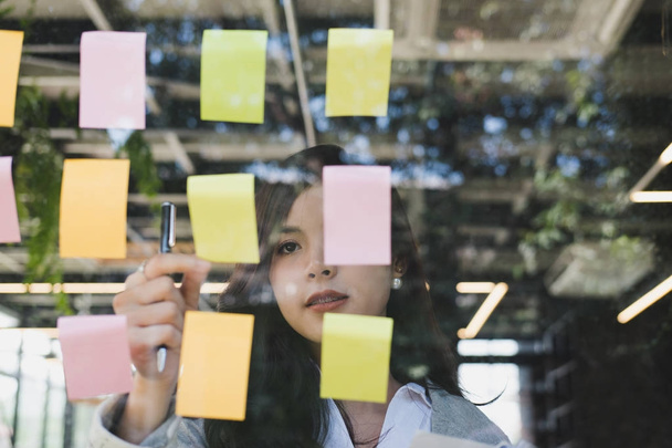 Empresária ler notas adesivas na parede de vidro na sala de reuniões
. - Foto, Imagem