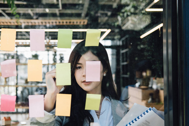 Businesswoman write on adhesive notes on glass wall in meeting r - Photo, Image