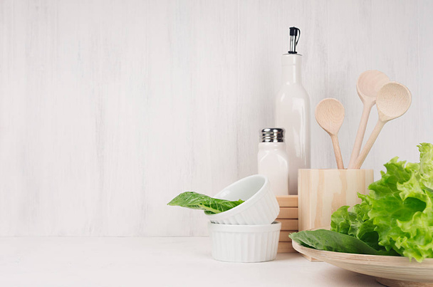 Elegant light kitchen interior with wooden utensils, ceramics and green leaves greens on white wood shelf. - Valokuva, kuva