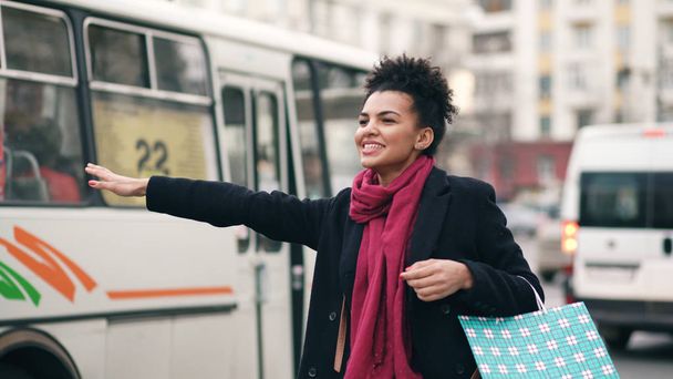 Attractive african american woman with shopping bags talking phone while waiting for taxi cab and coming back from mall sales - 写真・画像