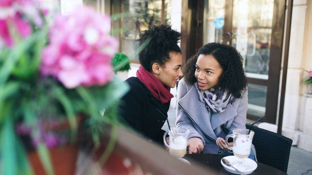 Two attractive mixed race female friends sharing together using smartphone in street cafe outdoors - Foto, immagini