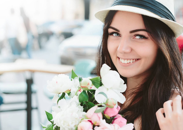 Close up portrait of young happy girl with flowers bouquet in outdoor cafe,smiling young woman.Cheerful red hair girl,style, lifestyle.Wearing dress and white hat. - Zdjęcie, obraz