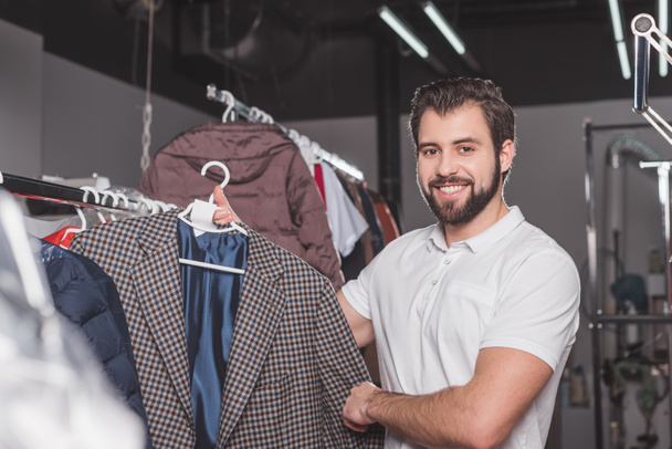 happy young dry cleaning worker hanging jacket at warehouse - Foto, Bild
