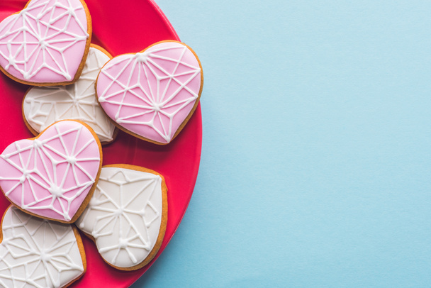 top view of glazed heart shaped cookies on pink plate isolated on blue - Valokuva, kuva