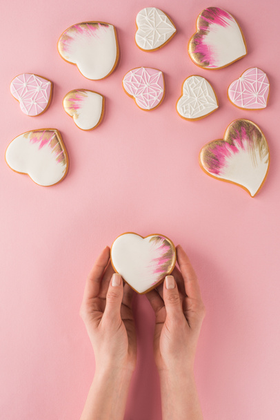 partial view of woman holding glazed cookie in hands isolated on pink, st valentines day concept - Foto, Imagem