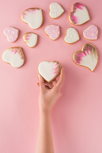 partial view of woman holding glazed cookie in hand isolated on pink, st valentines day concept - Φωτογραφία, εικόνα