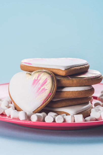 close up view of glazed cookies and marshmallow on pink plate isolated on blue - Photo, Image