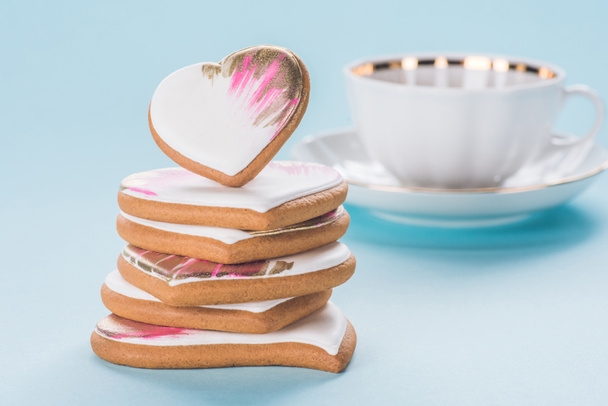 close up view of pile of glazed heart shaped cookies and cup isolated on blue, st valentines day concept - Fotografie, Obrázek