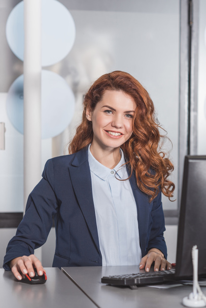 young smiling manageress using computerat workplace - Foto, afbeelding