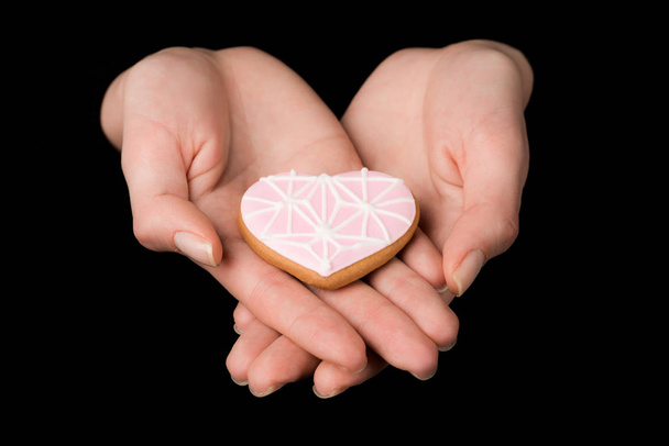 close up view of female hands with glazed heart shaped cookie isolated on black - Foto, immagini