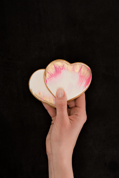 cropped shot of female hands holding glazed heart shaped cookies on dark backdrop, st valentines day concept - Foto, immagini