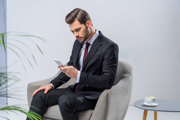 businessman sitting in armchair and looking at smartphone - Fotó, kép