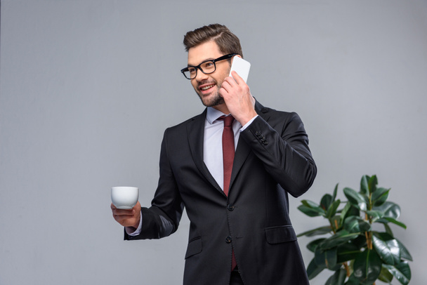 homem de negócios sorrindo falando por smartphone e segurando xícara de café
 - Foto, Imagem