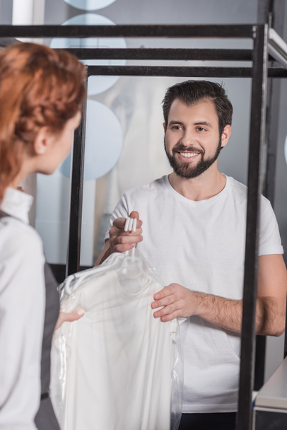 handsome young dry cleaning manager giving clothes to customer - Zdjęcie, obraz