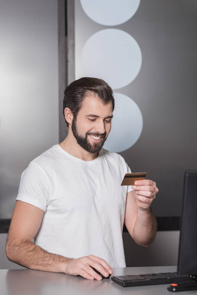 handsome young manager sitting at workplace with gold credit card - Foto, Bild