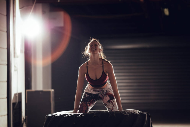Молода м'язиста жінка підкидає шину на перехресному тренуванні в гаражі
. - Фото, зображення