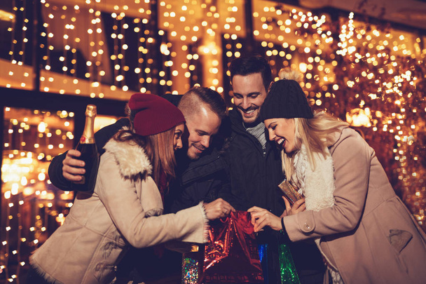 Deux jeunes couples joyeux s'amusent la nuit de Noël dans la rue de la ville avec beaucoup de lumières en arrière-plan
. - Photo, image