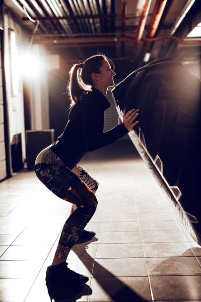 Giovane donna muscolare lanciando un pneumatico su cross fit formazione in garage
. - Foto, immagini