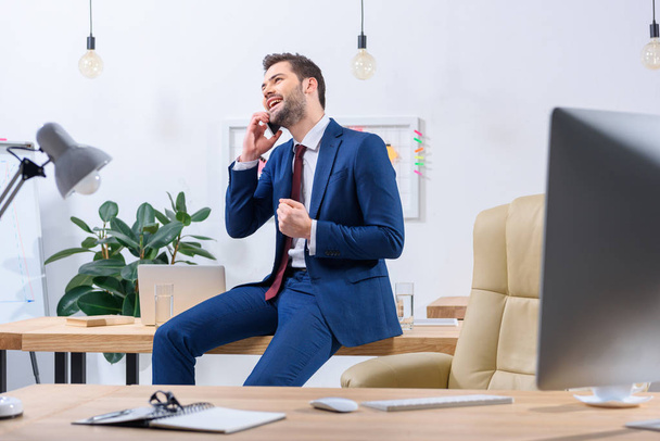 hombre de negocios feliz hablando por teléfono inteligente en la oficina y mostrando sí gesto
 - Foto, Imagen