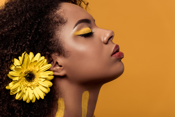 Stílusos afrikai-amerikai nő, művészi smink és haj álmodik, elszigetelt narancssárga háttér gerbera - Fotó, kép