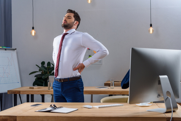 tired businessman standing and stretching in office - Zdjęcie, obraz