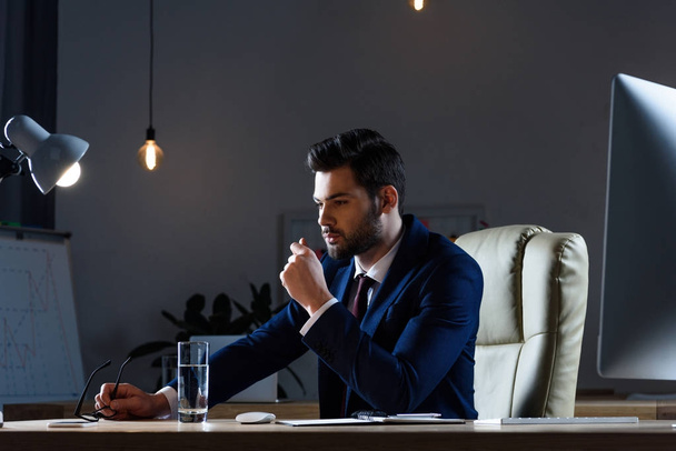 zamyšlený podnikatel sedí večer u pracovního stolu - Fotografie, Obrázek