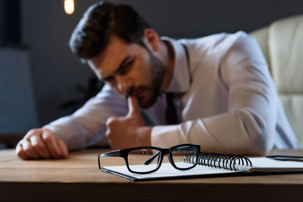 unavený zamyšlený podnikatel, opřel se o stůl s brýlemi na popředí - Fotografie, Obrázek