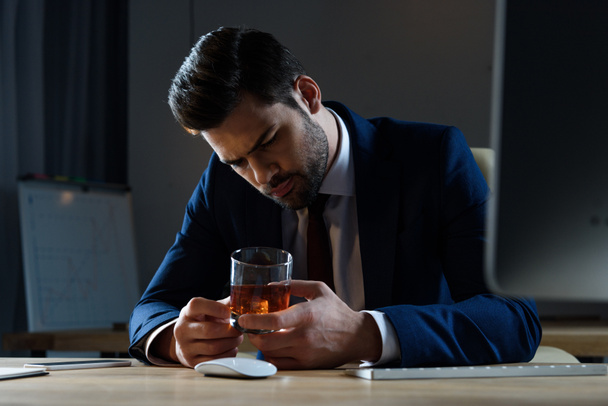 усталый пьяный бизнесмен смотрит на стакан виски в офисе
 - Фото, изображение