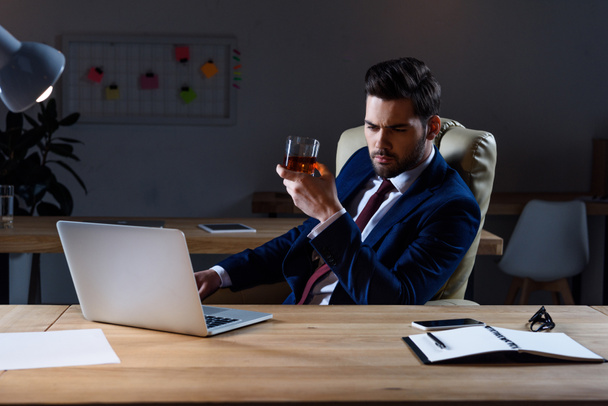 serious businessman sitting at laptop with glass of whiskey - Фото, зображення
