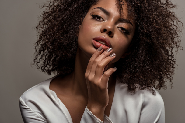 Mujer afroamericana tierna joven en camisa blanca con la mano en los labios aislados sobre fondo gris
 - Foto, Imagen
