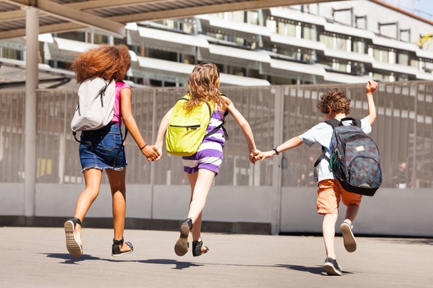 Lapset juoksevat kouluun kädestä pitäen ja reppuja päällään.
 - Valokuva, kuva