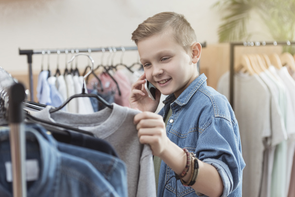 lachende jongen met smartphone terwijl doek in de hand bij shop   - Foto, afbeelding