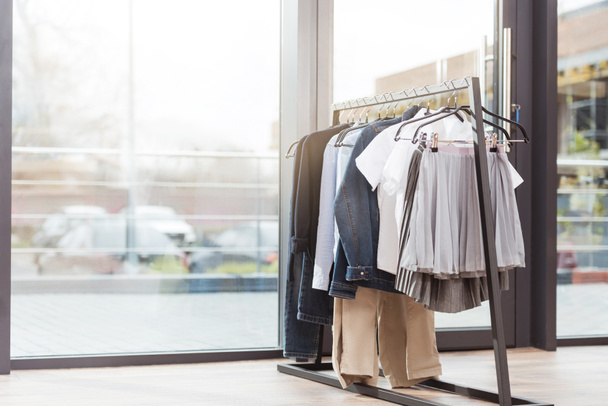 Различные одежды на hager в интерьере магазина против окна
  - Фото, изображение