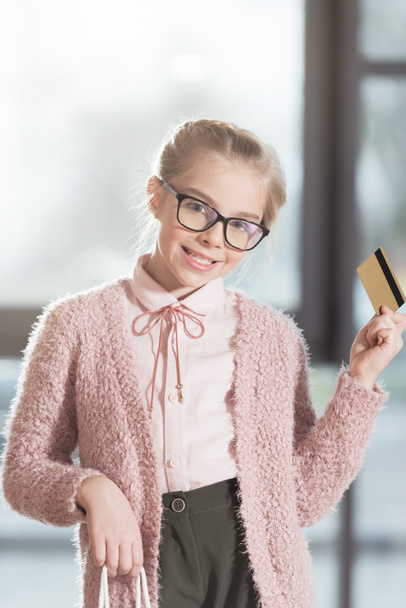 smiling child in glasses holding credit card at shop interior - Foto, Imagen