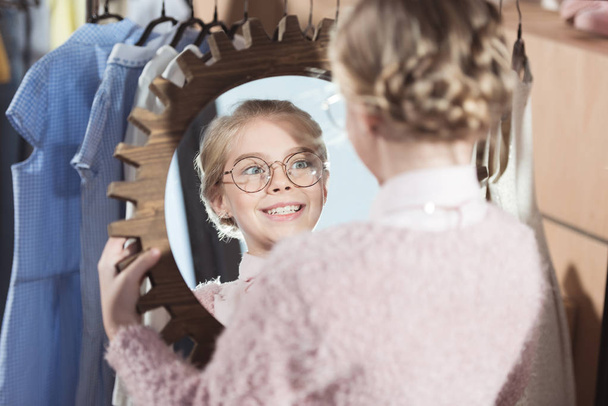 niña sonriente mirando el espejo en sus manos en el interior de la tienda
   - Foto, imagen