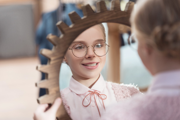 Улыбающийся ребенок смотрит в зеркало в руках в интерьере магазина
  - Фото, изображение