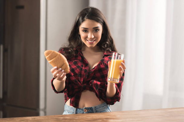 attractive young woman in checkered shirt holding croissant and orange juice for breakfast - Foto, imagen